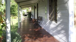 Un porche cubierto con suelo de madera, barandillas de metal y mobiliario exterior.