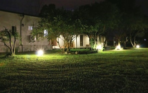 Un espacio exterior bien iluminado con césped, árboles y un edificio con porche.