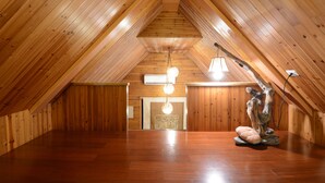 Un dormitorio en el ático con paredes de madera y techo inclinado. Se observa una araña colgando del techo y una escultura rústica sobre el suelo.