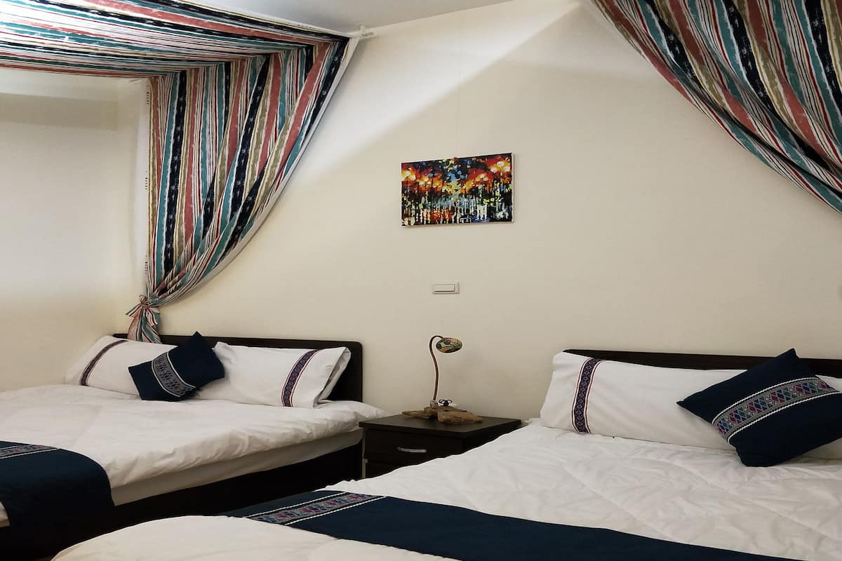 Una habitación de hotel con dos camas, cortinas a rayas, un cuadro en la pared y una mesita de noche con lámpara.