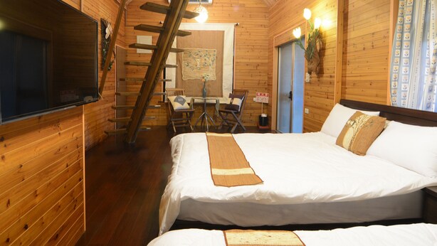 Acogedora habitación tipo cabaña de madera con una cama, una silla, una mesa y una escalera que lleva a un balcón.
