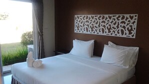 Un lit bien fait, avec du linge de lit blanc et des oreillers, un panneau décoratif au mur et une vue sur la verdure à l’extérieur.