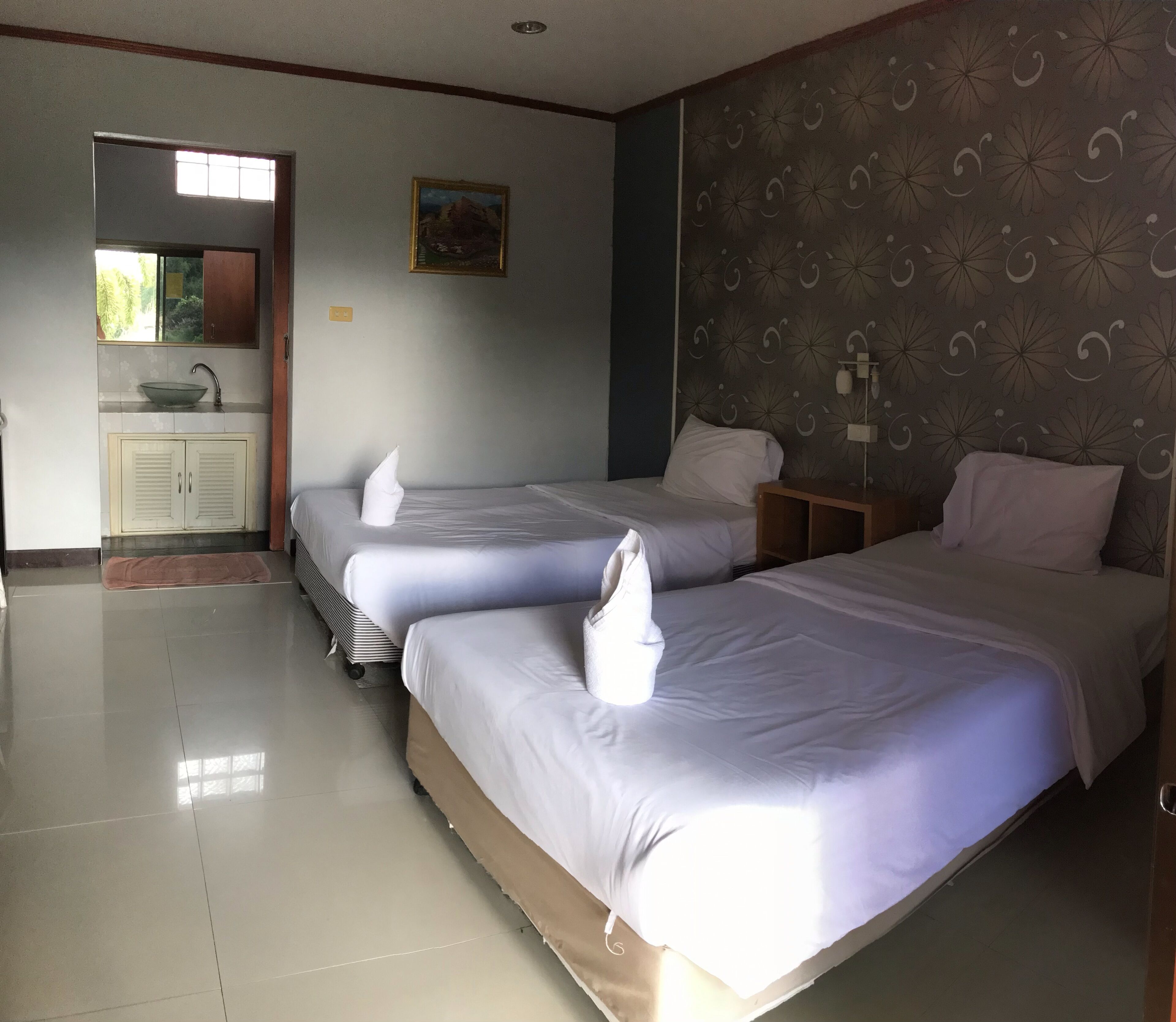 Habitación de hotel con dos camas, un baño con lavamanos y un cuadro en la pared.