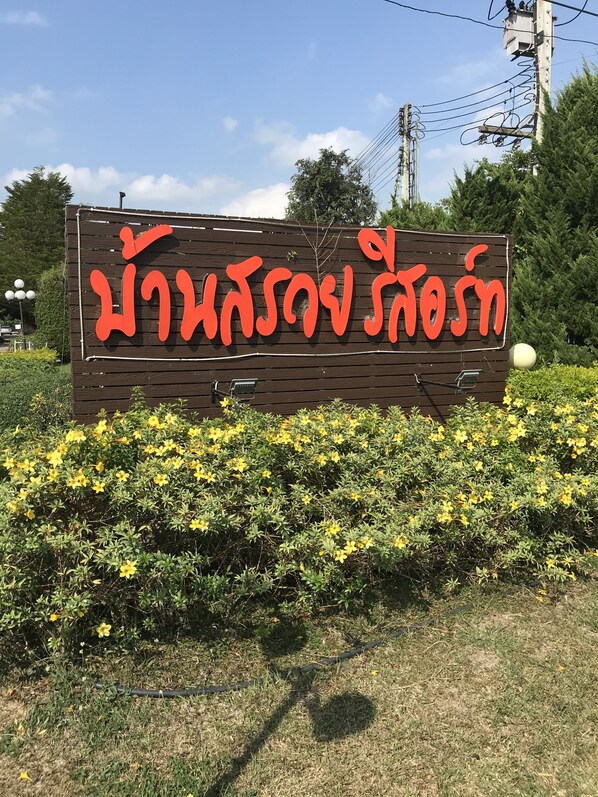 A wooden sign with red text, surrounded by yellow flowers and greenery. - Baan Saui Resort (Mae Suai)