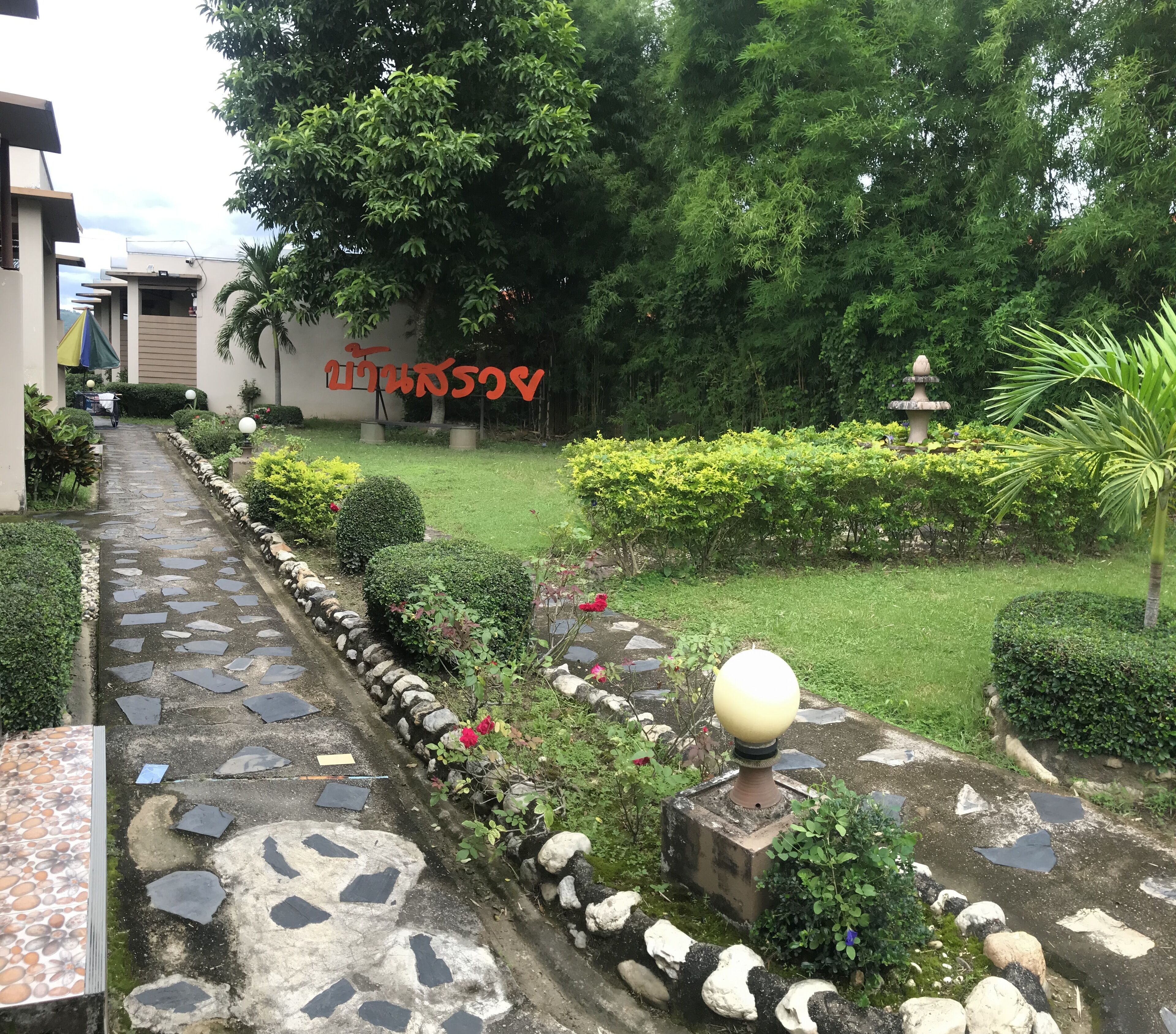 Un sendero de jardín con losetas de piedra, bordeado por rocas y plantas, que conduce a un edificio con un letrero en idioma extranjero.