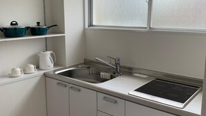 A modern kitchen with white cabinets, a stainless steel sink, a window above the sink, and a stove. - Hotel Oxio (Okayama)