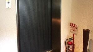 An elevator with a metallic interior, a fire extinguisher mounted on the wall, and a fire safety sign. - Hotel Oxio (Okayama)