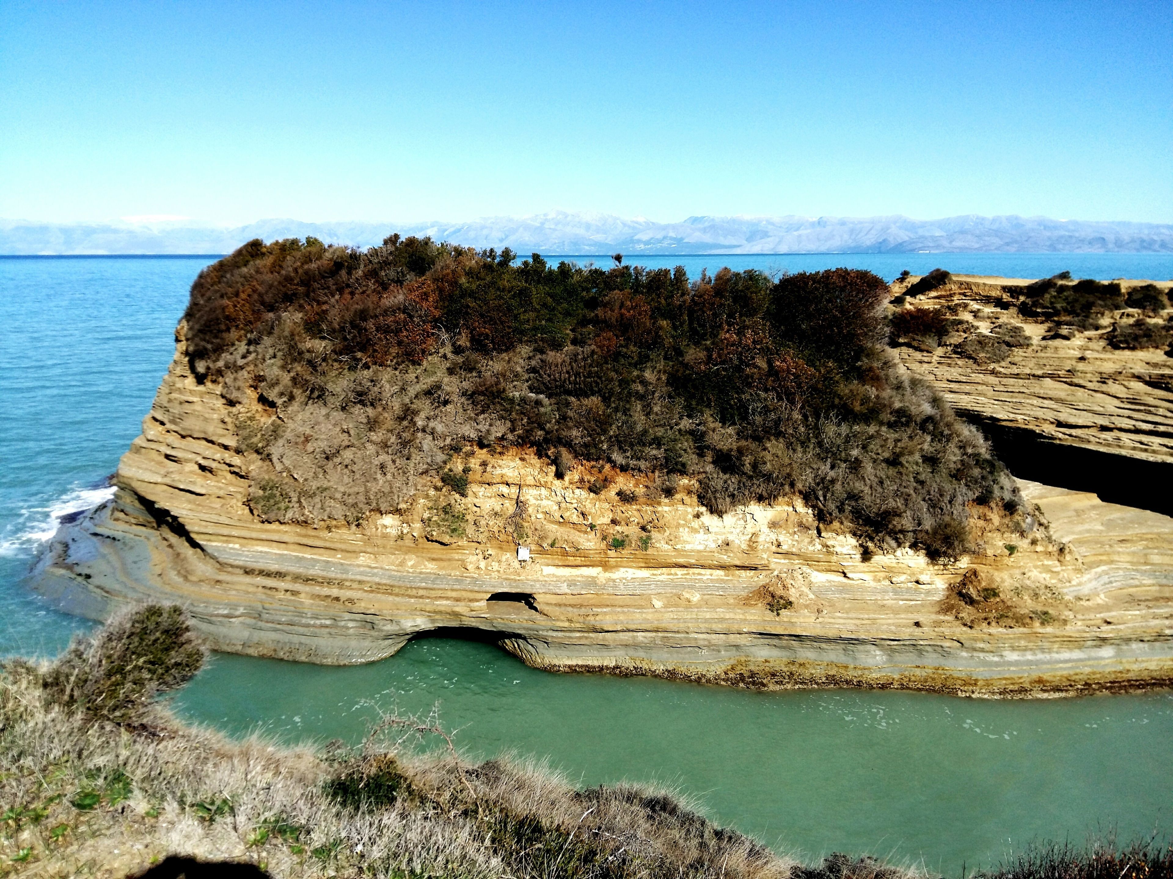 A coastal cliff with layered rock formations and a clear view of the sea.