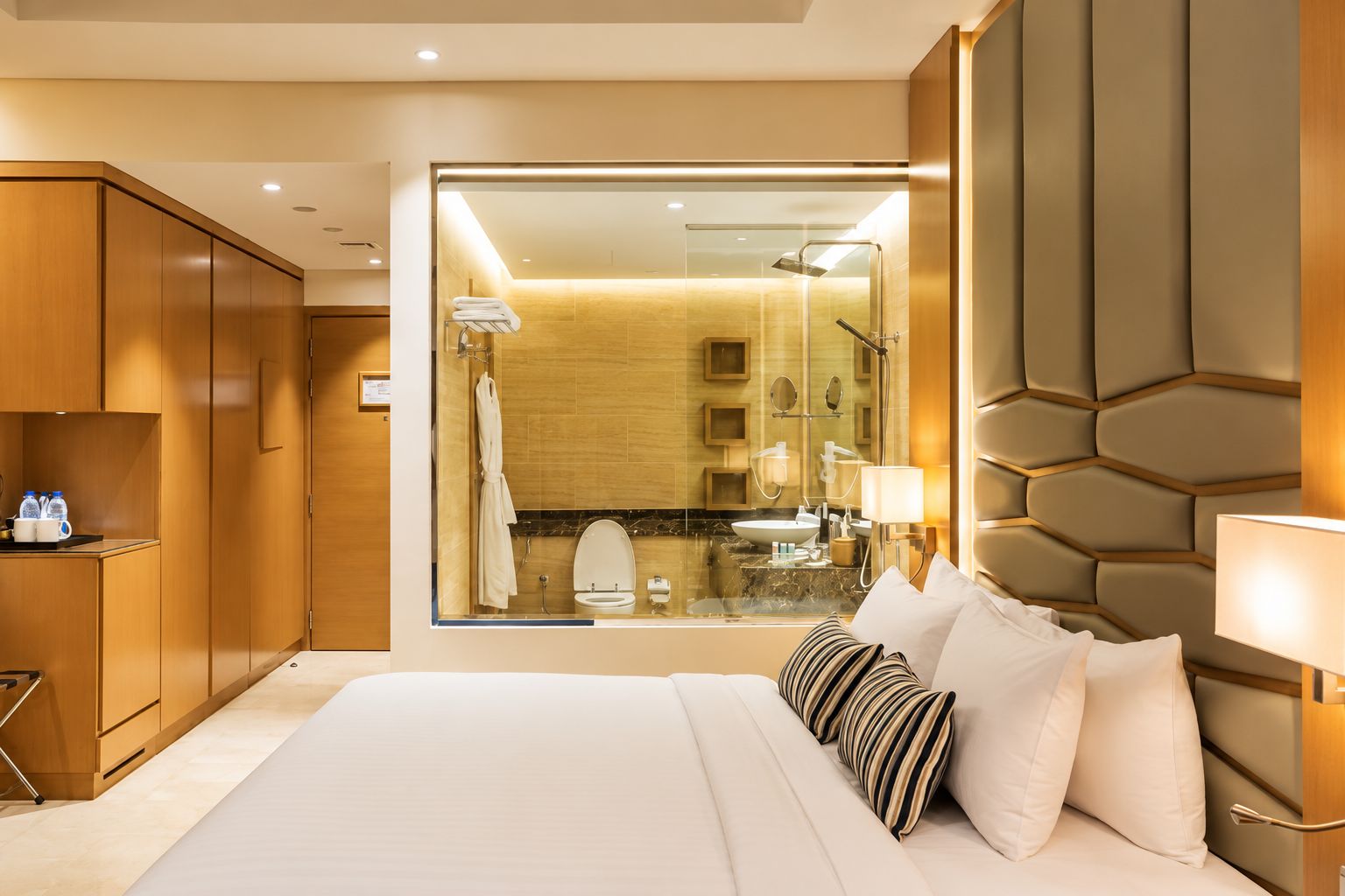 Une chambre d’hôtel dotée d’un grand lit, d’une armoire en bois, d’une salle de bain avec un mur en verre et d’un design moderne.