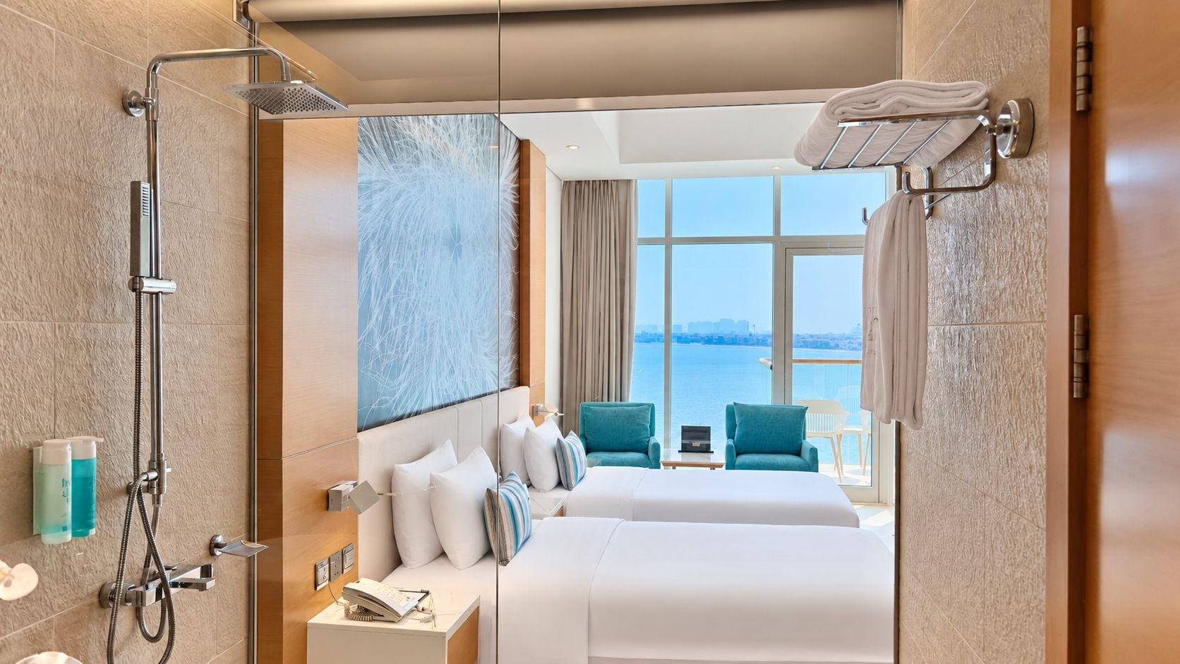 A hotel room with a shower, a bed, two chairs, a view of the sea, and a window.