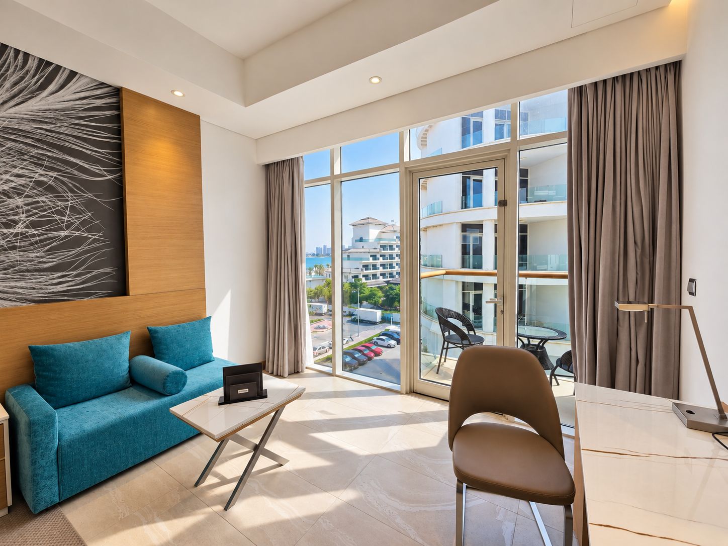 Ein modernes Hotelzimmer mit einer Couch, einem kleinen Tisch, einem Sessel und Blick auf die Stadt durch große Fenster.