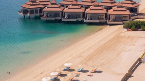 Un resort frente a la playa con bungalows sobre el agua, una playa de arena y una vista despejada del mar.