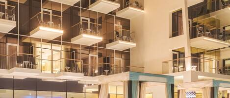 A modern hotel interior with a swimming pool, multiple balconies, and a high ceiling with geometric lighting fixtures.