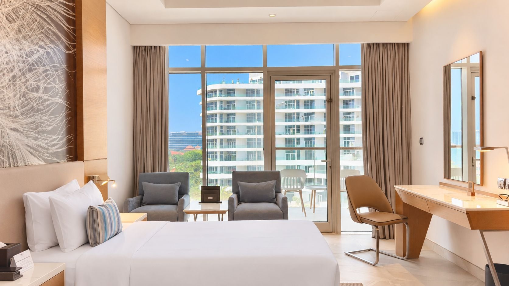 Een hotelkamer met een bed, twee fauteuils, een bureau en een groot raam met uitzicht op wolkenkrabbers.