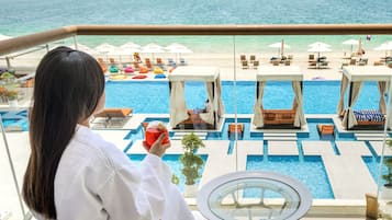 A balcony with a pool, lounge chairs, and umbrellas.