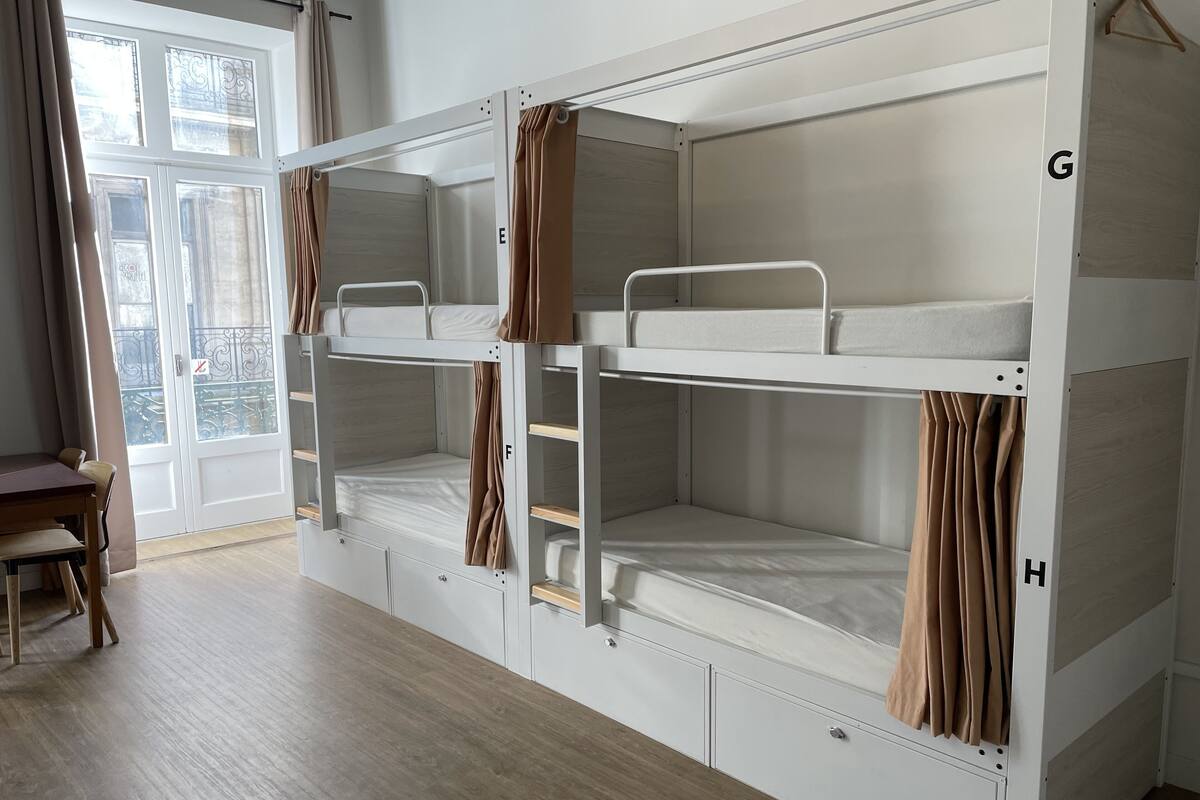 A bunk bed room with a wooden floor, a desk, and a view of the outside through a door.