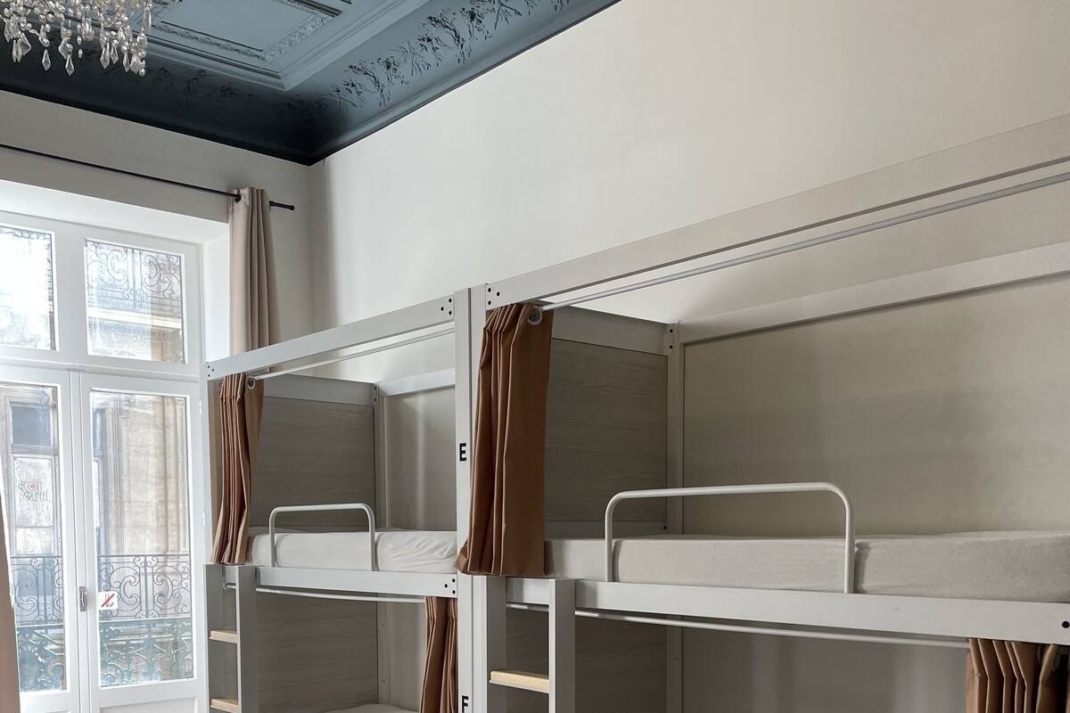 A room with bunk beds, a chandelier, and a view through a window with curtains.