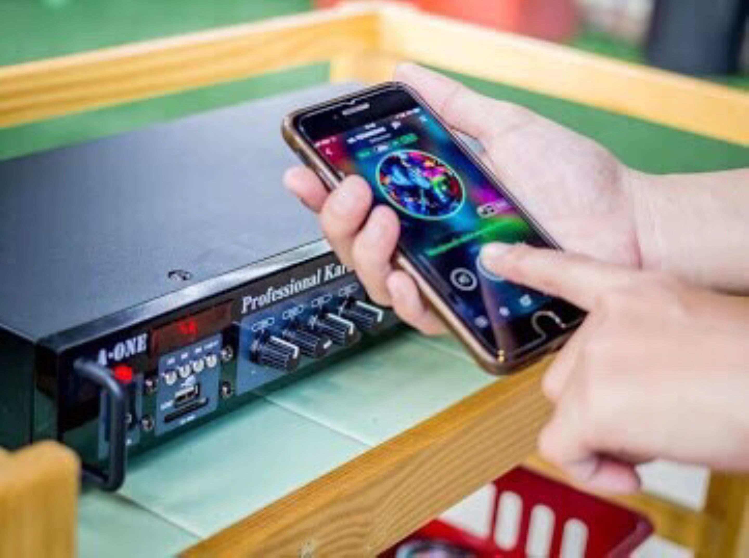 Una persona tiene in mano uno smartphone con un'interfaccia colorata, in piedi accanto a un dispositivo elettronico nero etichettato 'Professional Kan'.
