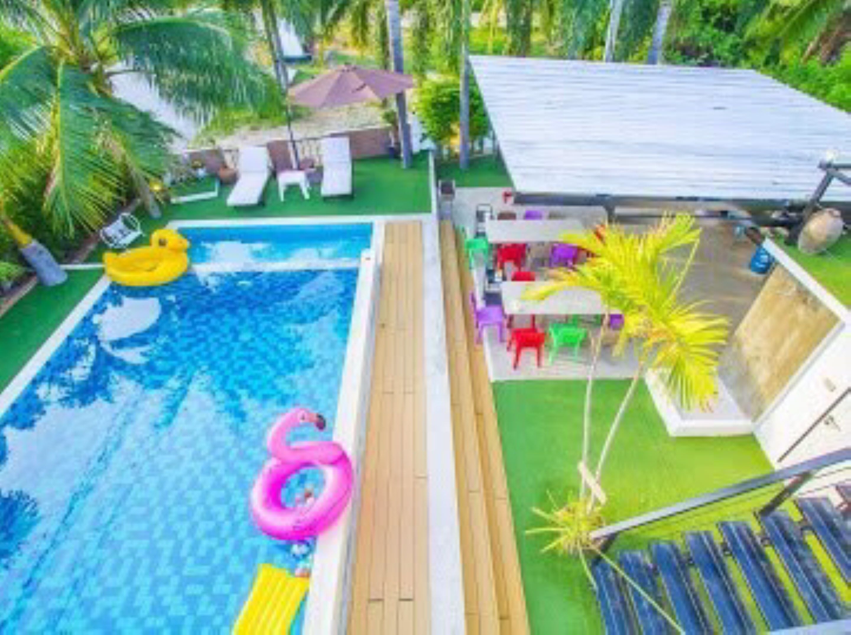 A swimming pool with inflatable toys, a wooden deck, and a covered seating area with chairs and tables.