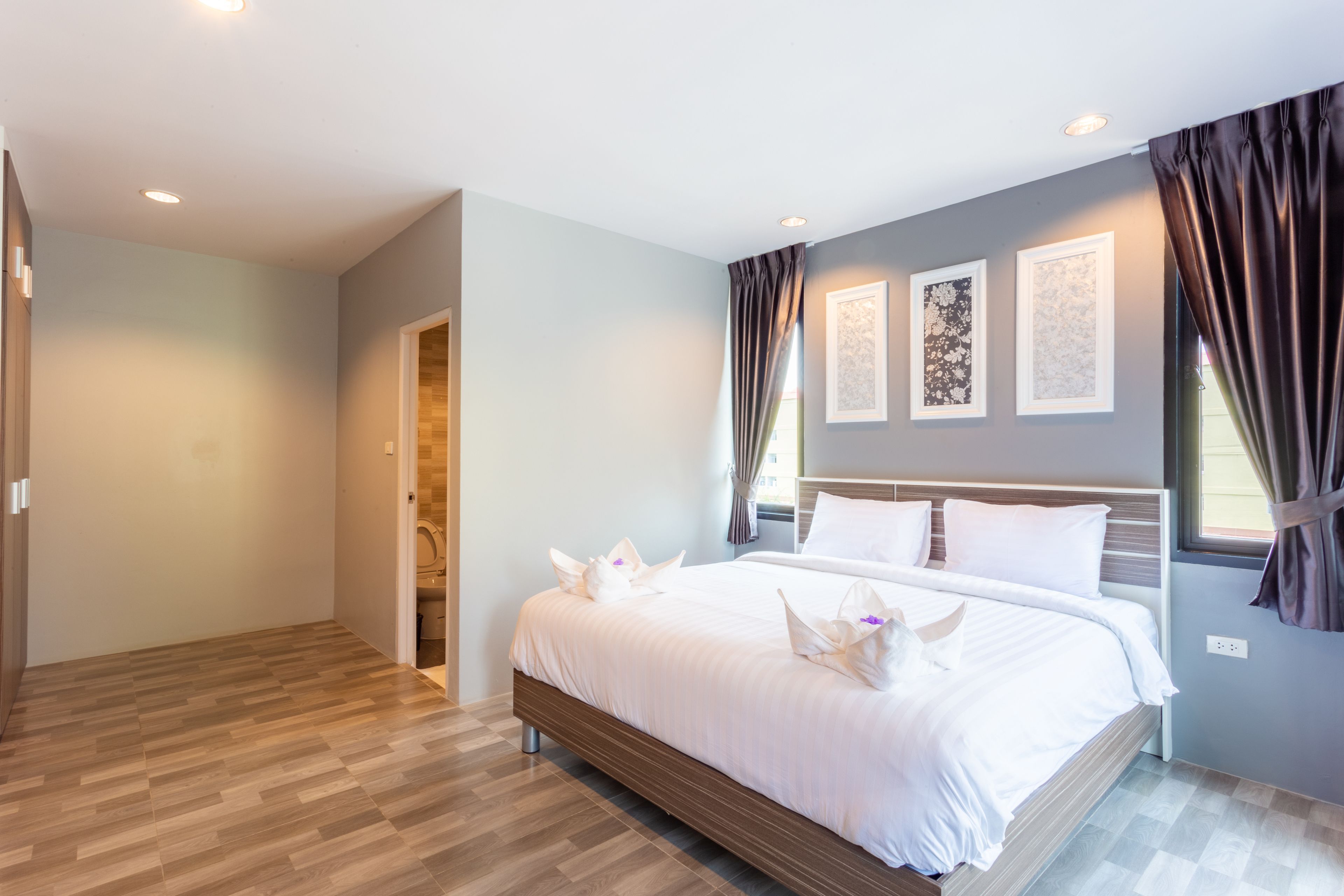A modern hotel room with a large bed, wooden flooring, and a view of the city.