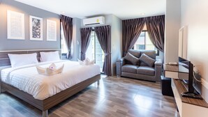 A modern hotel room with a large bed, a sofa, and a desk with a computer. - Grand Inter Hotel (Samut Sakhon)