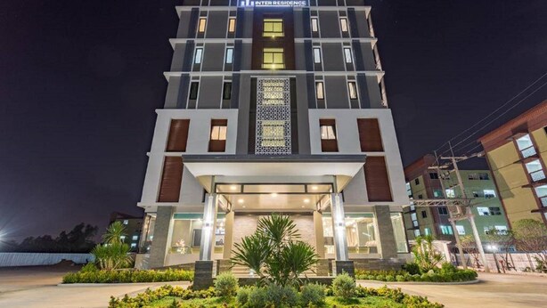 A multi-story hotel with a modern facade, a central entrance with a decorative screen, and a well-lit exterior. - Grand Inter Hotel (Samut Sakhon)