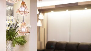 A reception area with a brown leather sofa, a vase with white flowers, and geometric pendant lighting. - Grand Inter Hotel (Samut Sakhon)
