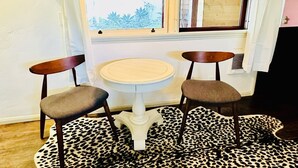 A dining area with a round table and two chairs, a leopard print rug, and a window with curtains.
