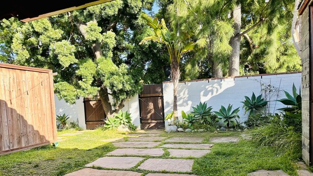 A garden with stone pathways, a wooden fence, and various plants.