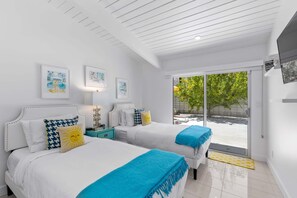 A modern hotel room with two beds, a large sliding glass door to the outdoors, and artwork on the walls.