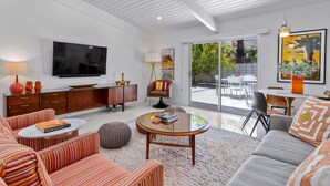 A modern living room with a flat-screen TV, striped sofas, a glass coffee table, and a dining area with a view.