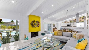 A modern living room with a glass coffee table, a sofa, and a yellow accent wall.