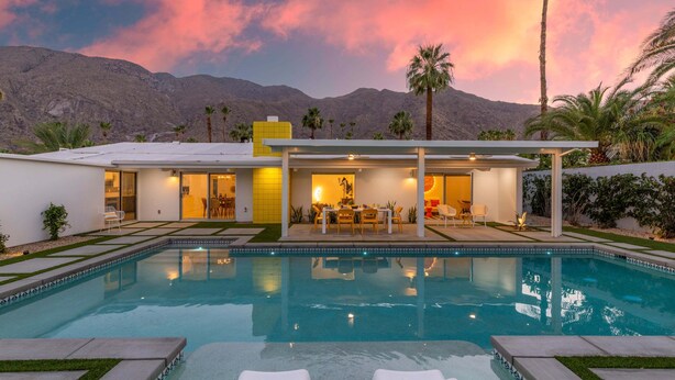 A modern house with a swimming pool, patio, and mountain backdrop.