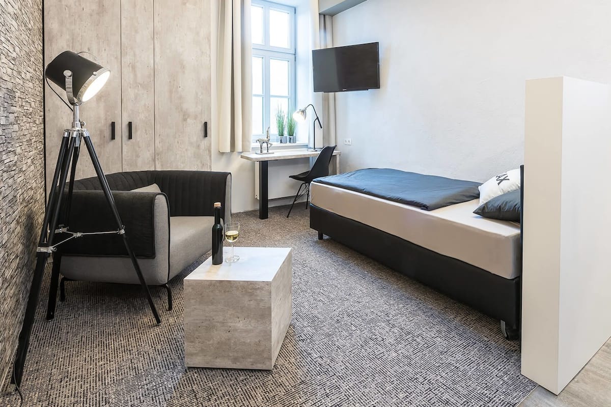 A modern hotel room with a bed, a desk, a chair, a lamp, and a TV.