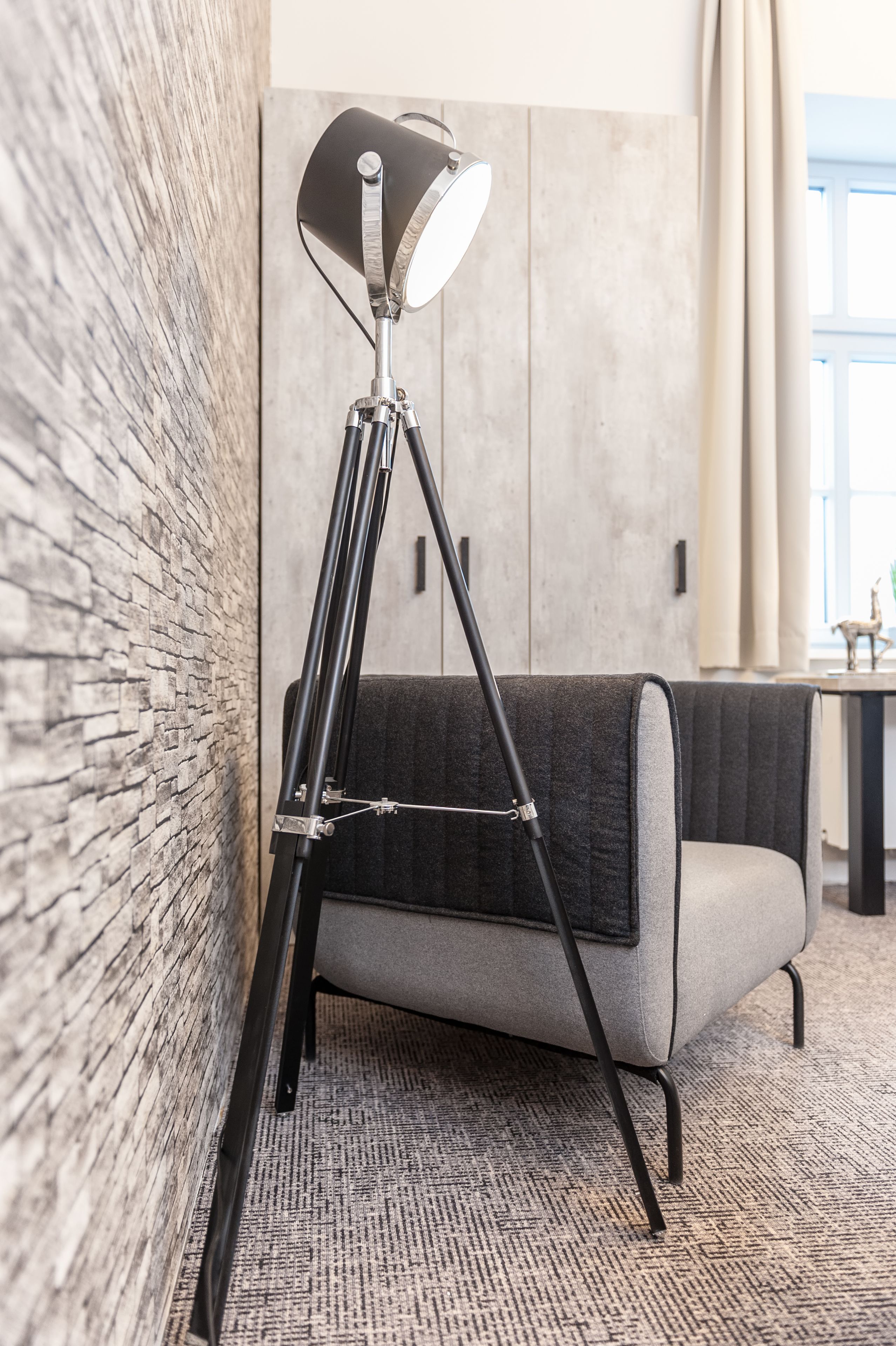 A modern room with a tripod floor lamp, a grey sofa, and a textured carpet.