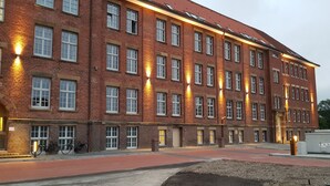 A large brick building with multiple windows and a paved area in front.