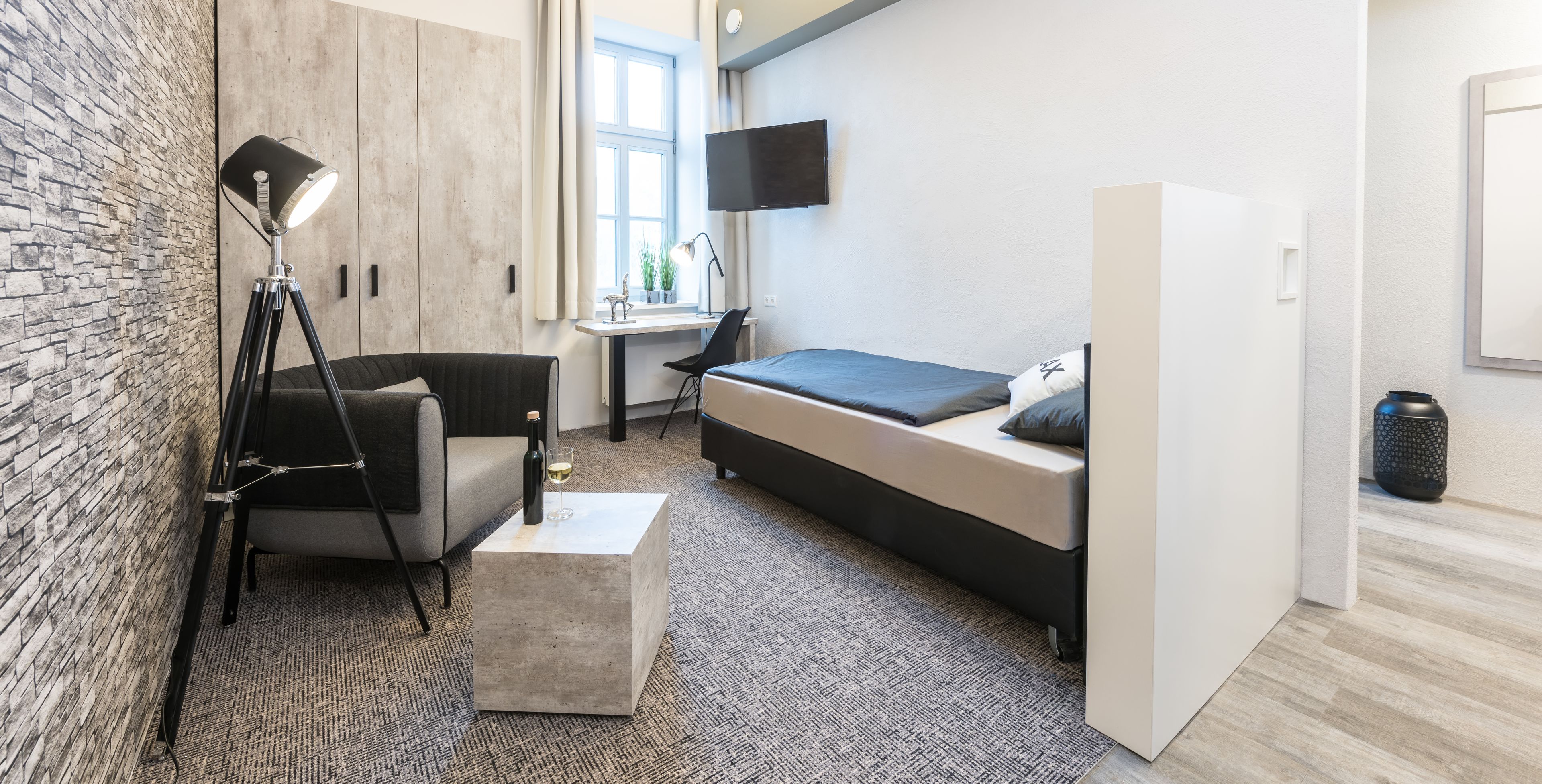A modern bedroom with a bed, a desk, a chair, a lamp, and a TV.