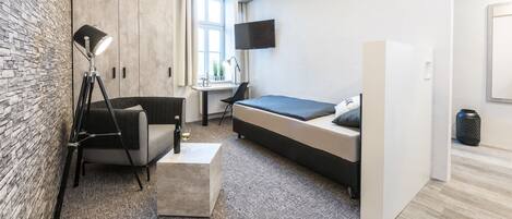 A modern bedroom with a bed, a desk, a chair, a lamp, and a TV.