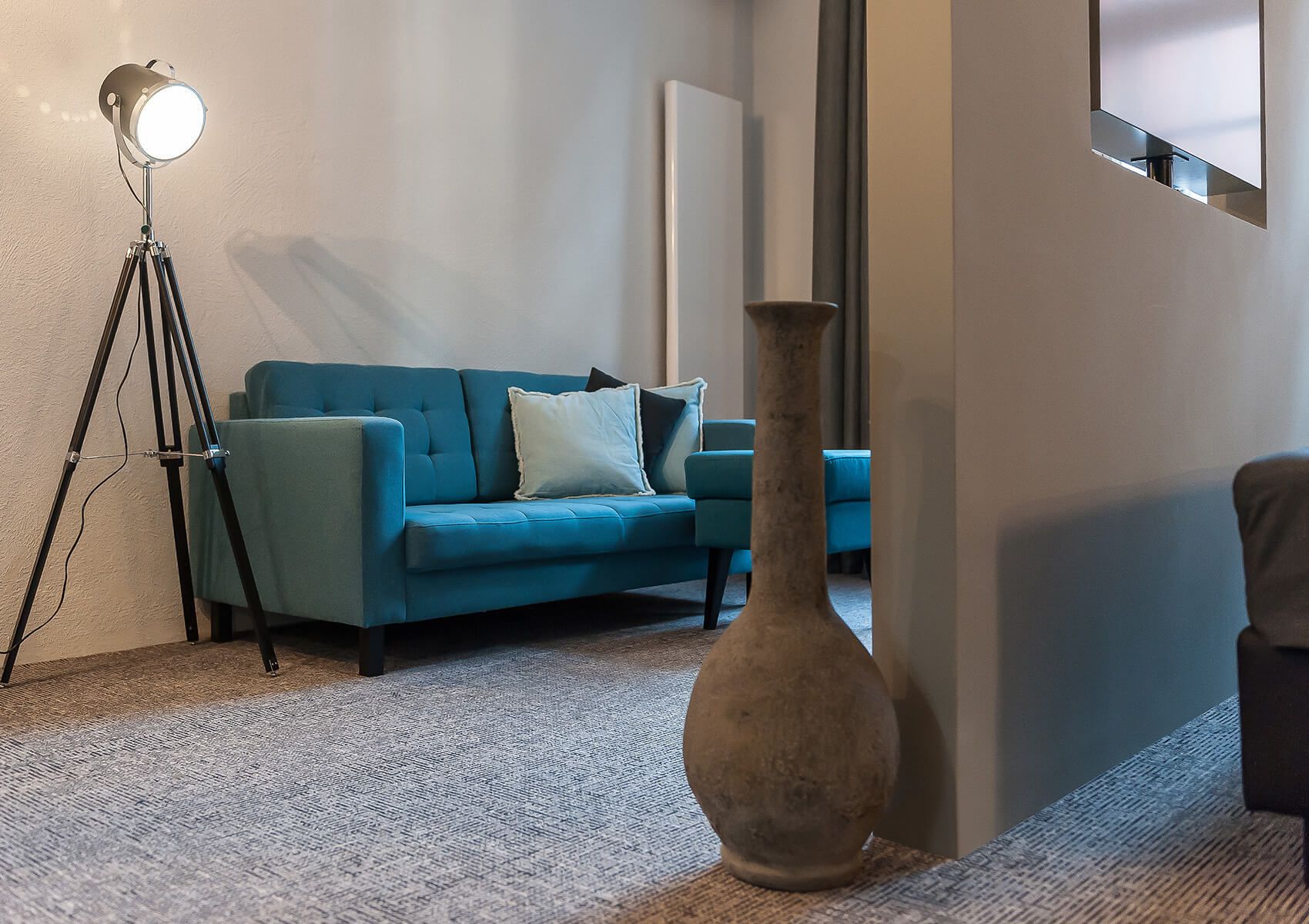 Een moderne woonkamer met een blauwe bank, een grote vaas en een vloerlamp.