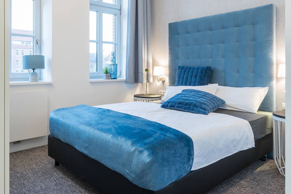 A hotel room with a large bed, a bedside table, a lamp, and a window with curtains.