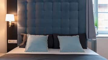 Un dormitorio con cabecera capitonada, dos almohadas, una lámpara de noche y una ventana con cortinas.