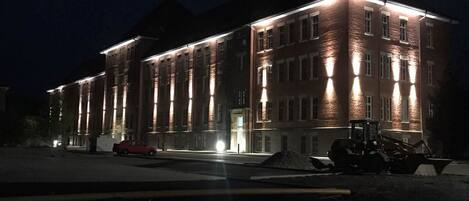 A large brick building with multiple windows and a well-lit facade at night.