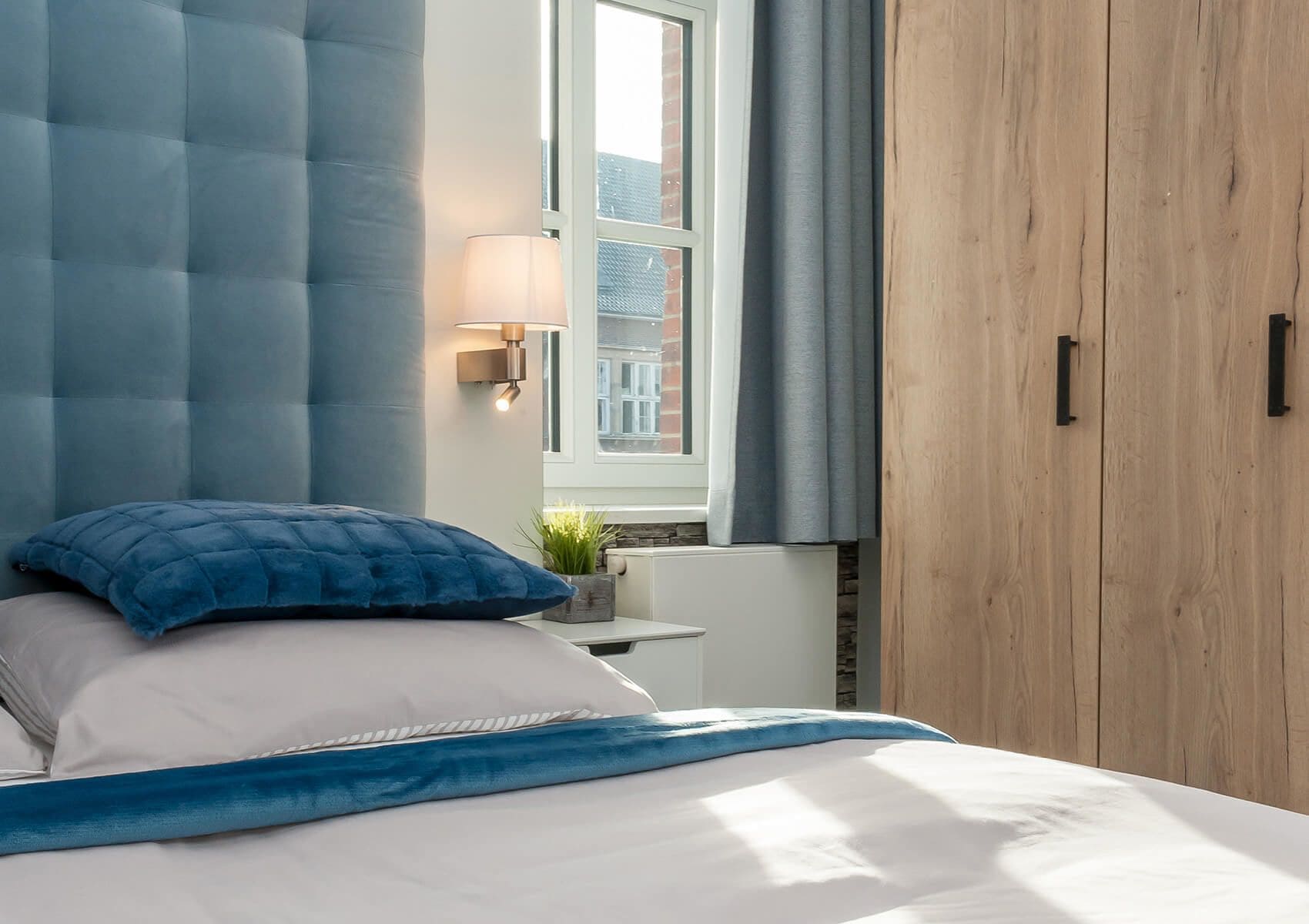 Un dormitorio con cama, ventana con cortinas, mesita de noche con lámpara y armario.