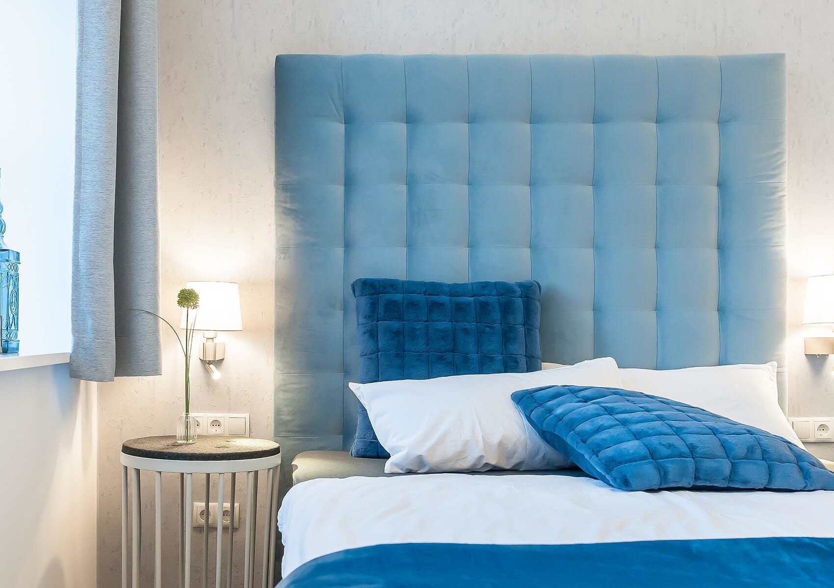 Un dormitorio con un gran cabecero capitonado, una mesita de noche redonda y ropa de cama azul.