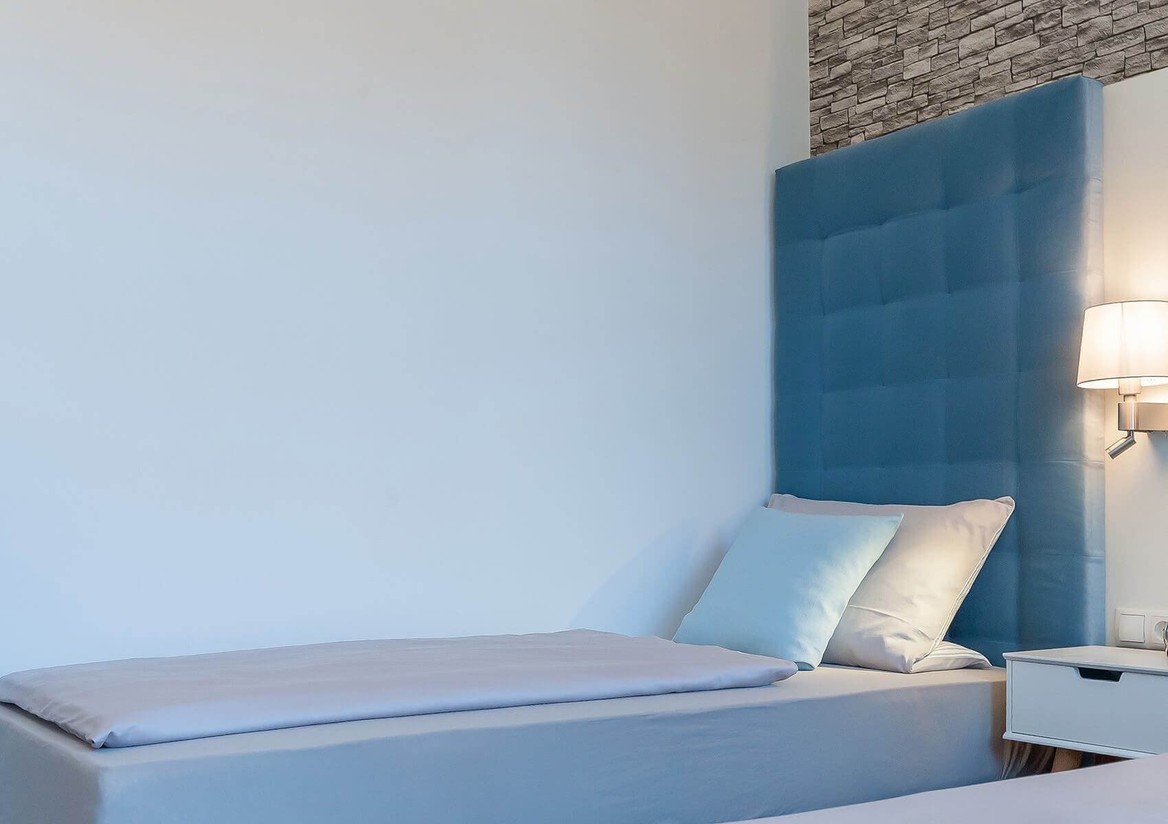 Un dormitorio moderno con cabecera azul, una mesita de noche y una lámpara de pared.