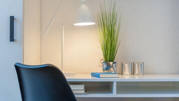 A modern desk with a white lamp, a blue book, and a plant in a reflective vase.
