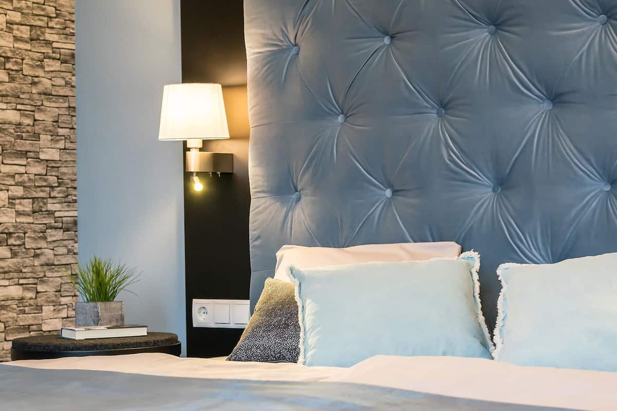 A modern bedroom with a tufted headboard, a bedside lamp, and a stone accent wall.