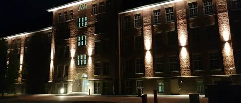 Un edificio grande de varios pisos con ventanas iluminadas y una entrada principal.