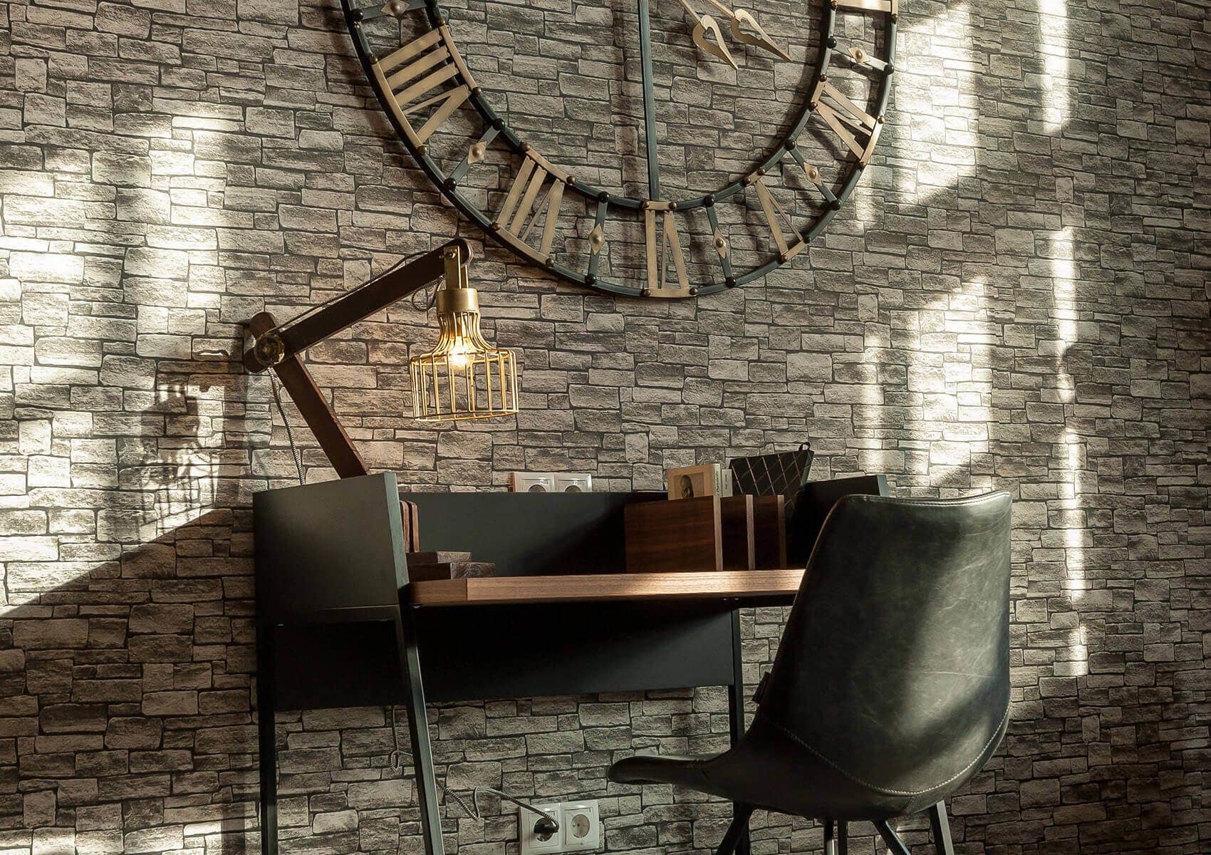 Un ambiente di lavoro moderno con parete in mattoni, un orologio grande, una scrivania con sedia e una lampada a sospensione.