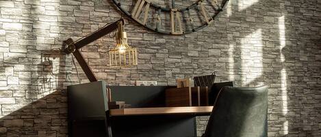 A modern workspace with a brick wall, a large clock, a desk with a chair, and a hanging light fixture.